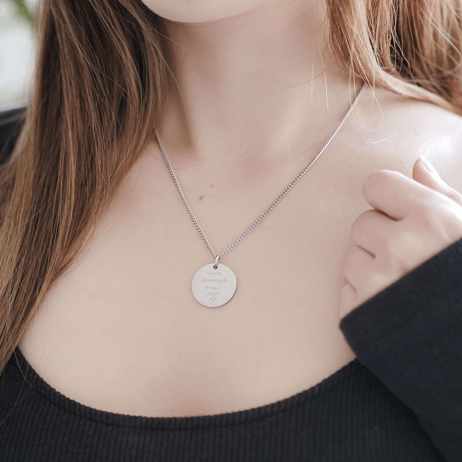 woman wearing silver disc shaped necklace engraved with a loved ones handwriting